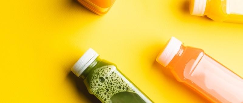 Colourful juices in plastic bottles against a yellow background.