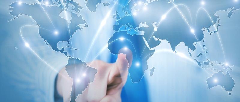 Hand touching a digital world map with glowing connection lines linking continents on a blue background.