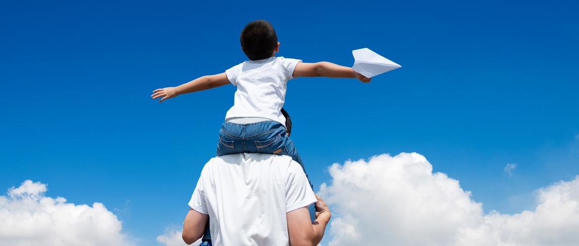 Son sitting father's shoulder and throwing paper plane