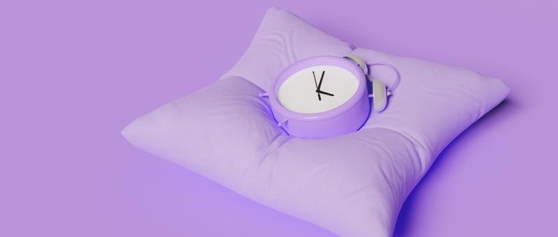 Purple alarm clock face-up on a purple pillow against a purple background.