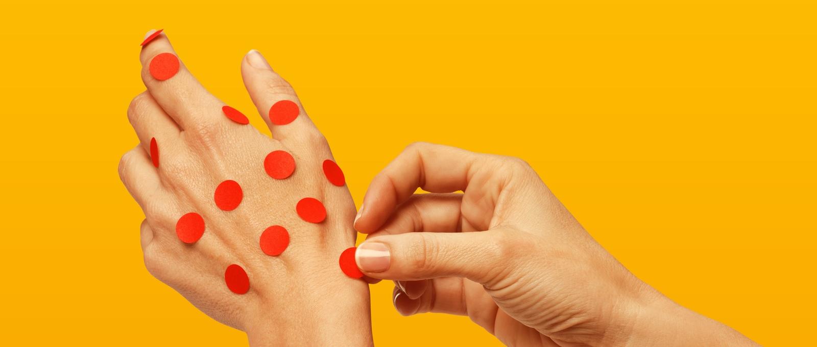 Hand Sticking red polka dots on another hand, red spots.