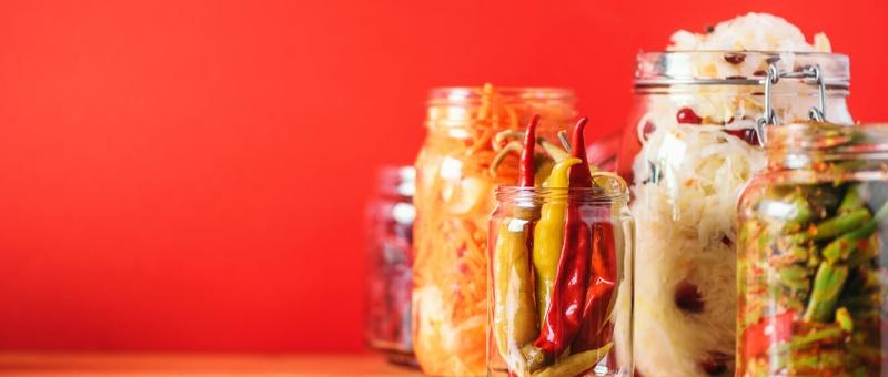 Assorted probiotic foods in lidless, clear glass jars against red background.