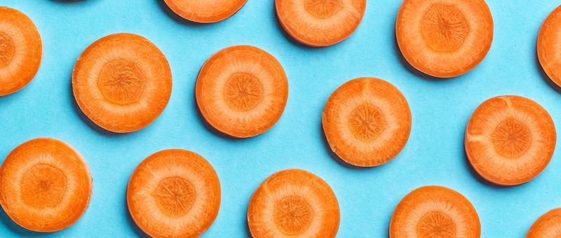 Fresh carrot slices arranged in a pattern on a bright blue background, showing their vibrant orange circular shapes.
