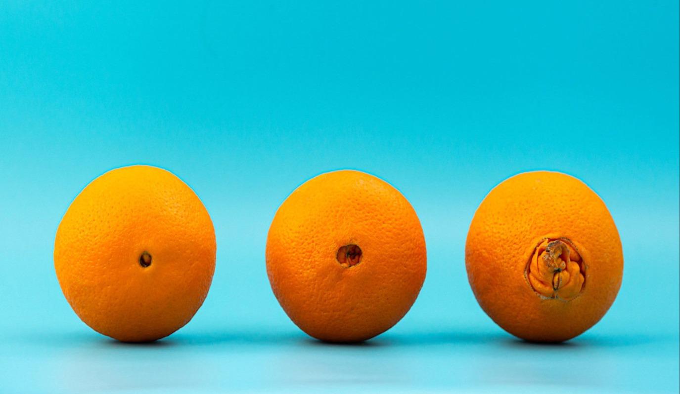 Three oranges in a row against a turquoise background, showing progressive damage to their navels from left to right.