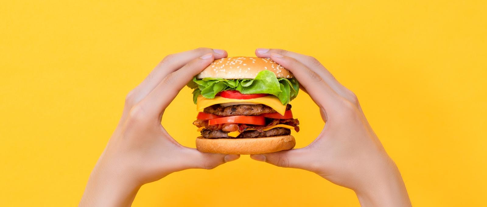 Hands holding burger on yellow isolated background