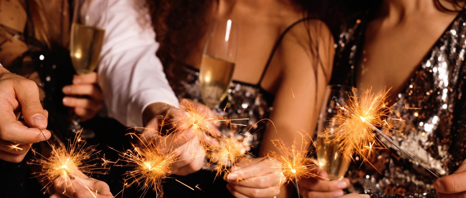 Friends with glasses of sparkling wine and sparklers celebrating New Year, closeup
