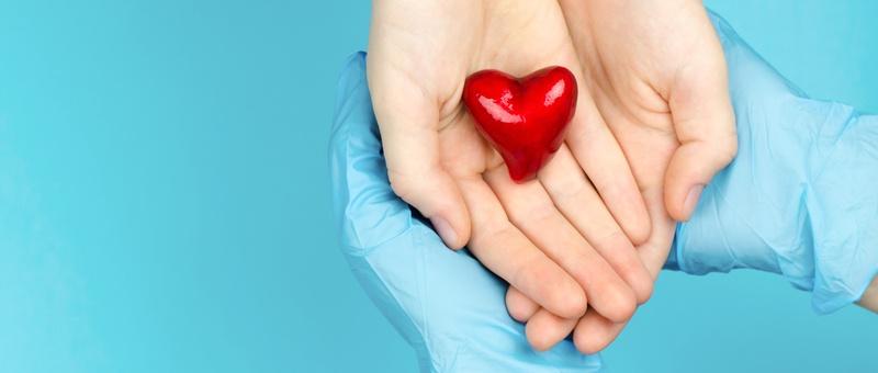 Patient and healthcare provider with gloved hands holding red shiny heart together against blue background.