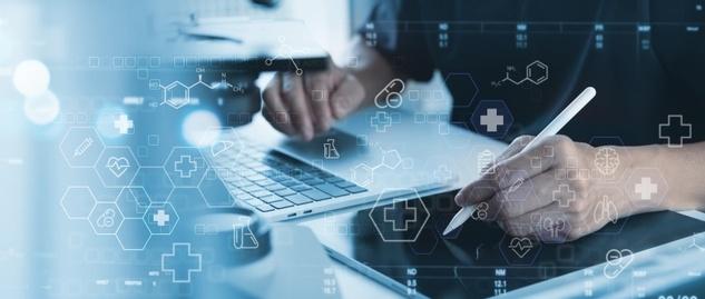 Person working on laptop and digital tablet with medical icons and healthcare graphics overlaid in blue tones.