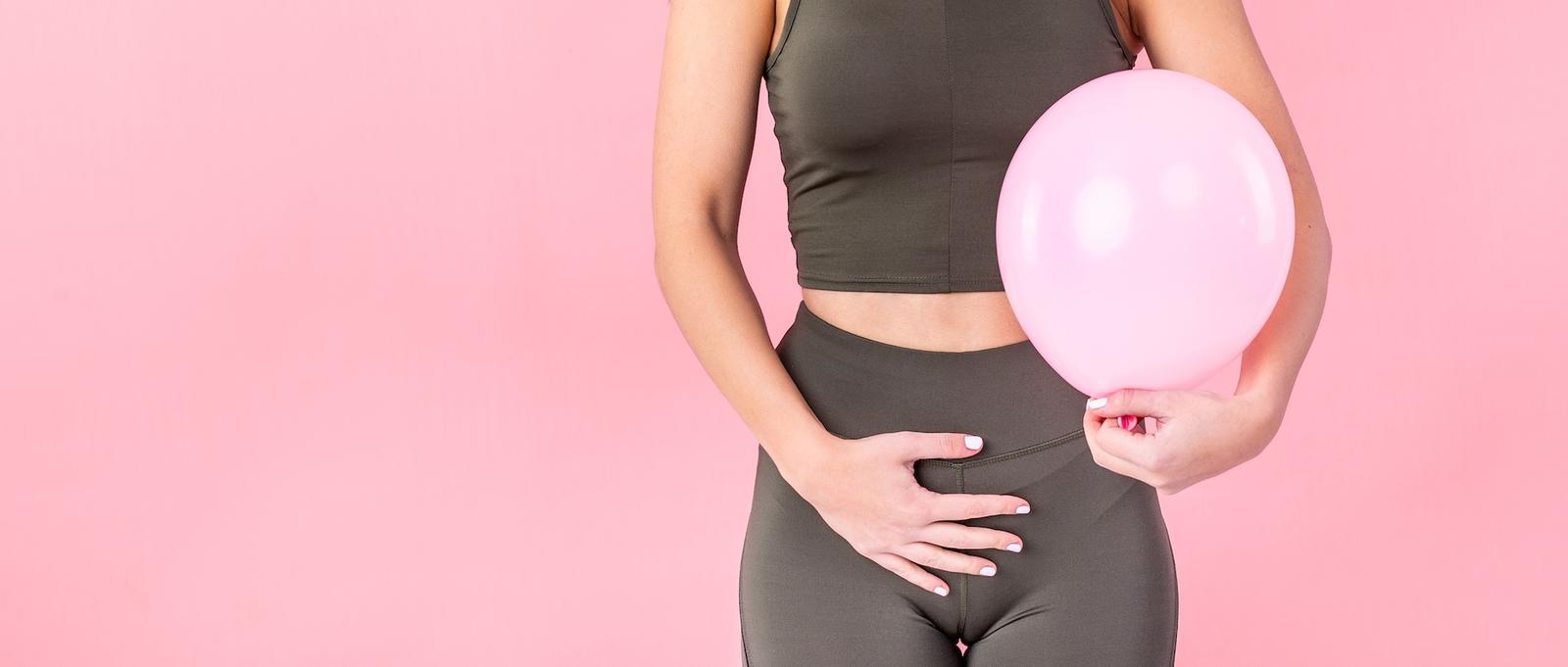 A close up of a woman holding her stomach with her right hand and holding a pink balloon in her left hand. The image conceptualises an ectopic pregnancy.