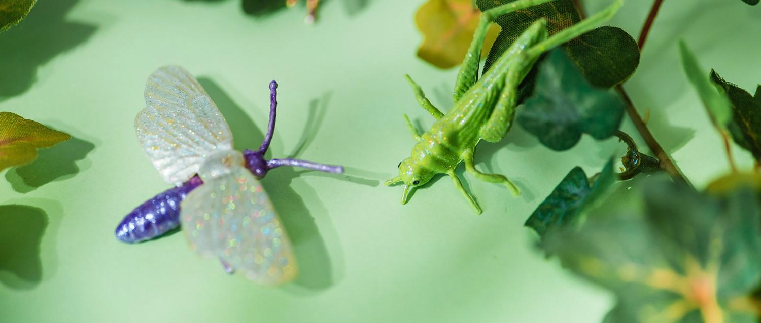 Decorative toy insects on a green surface - a purple butterfly with sparkly wings and a bright green praying mantis.