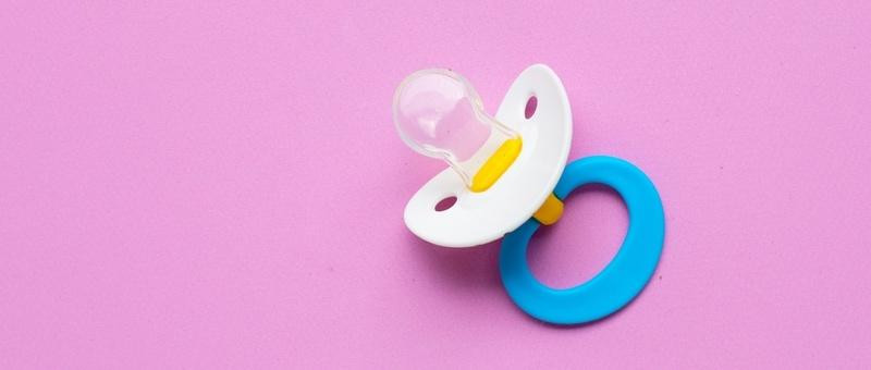 Blue baby pacifier against purple background.